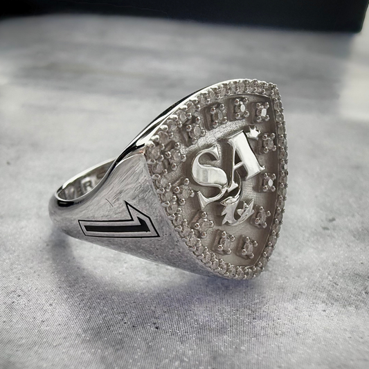 A Close up shot of a Initial signet ring in white gold on a grey textured background