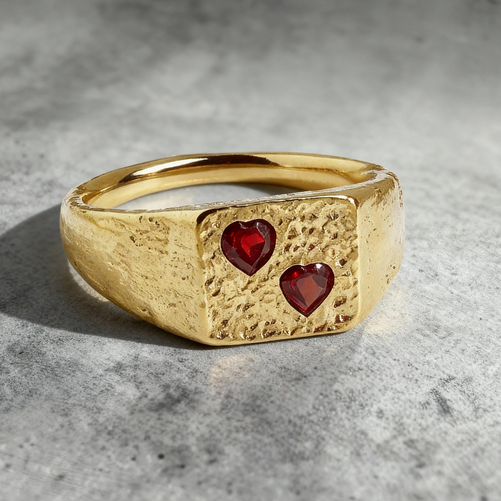 this is an eye level close up shot of a custom 18ct red ruby gemstone signet ring on a grey textured background
