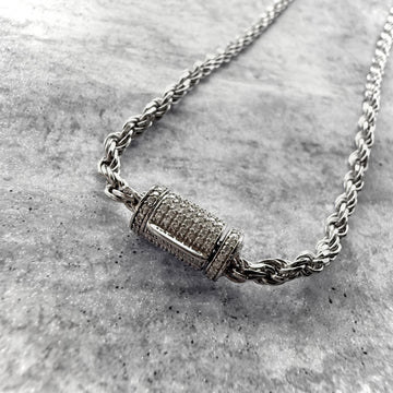 A close up shot of a custom made rope chain in 18k white gold, with a custom diamond barrel clasp. on a grey textured background