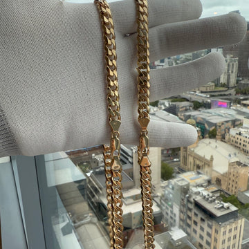 two Gold Curb Chains 8mm width being held whilst wearing a white glove with a city view background
