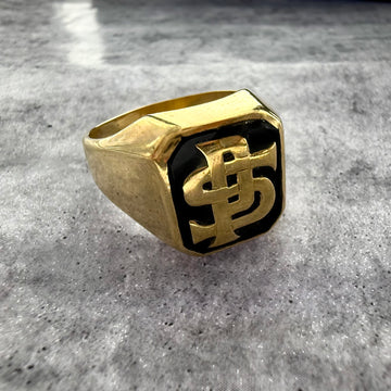 This is a custom initial P & S signet ring in yellow gold with a black enamel background. on a grey textured background