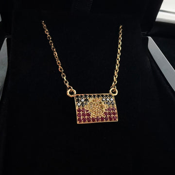 A high angle photo of a custom 18k yellow gold aboriginal flag pendant with natural black diamond, Yellow sapphire and red ruby gemstones, laid on a black background