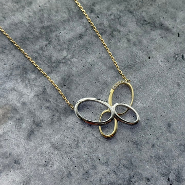 Close up shot of a custom two tone butterfly pendant & necklace on a grey textured background.