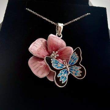Front shot of a custom butterfly and flower pendant with a necklace on a black backrgound