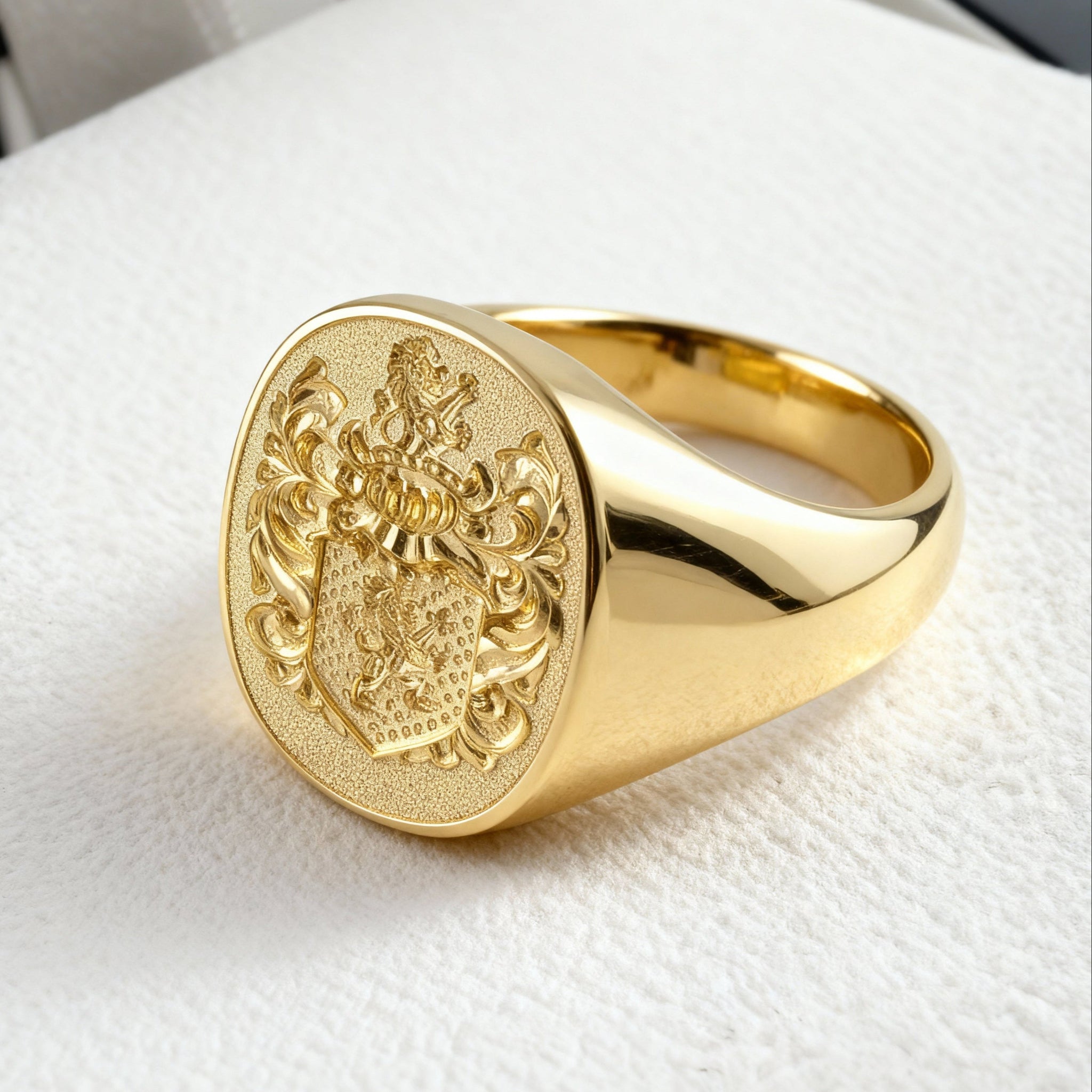 This is a close up shot of a custom coat of arms signet ring in 18k yellow gold on a wool textured cream colour background
