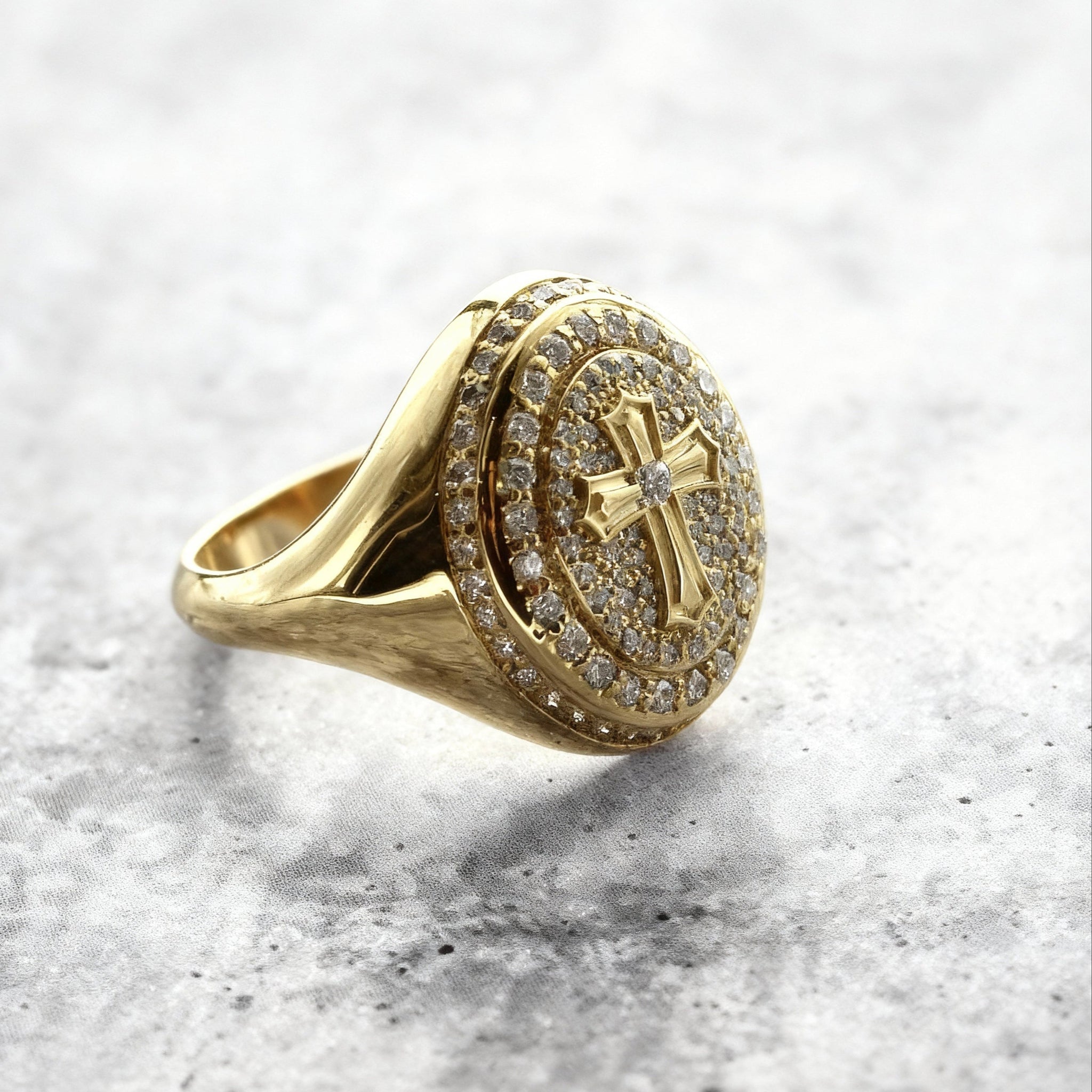 A close up eye-level shot of a Custom Gold Cross signet ring with natural diamond on a grey textured background