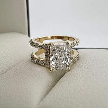 front angle photo of a 1.5ct radiant cut diamond ring in yellow gold on a white and cream textured background
