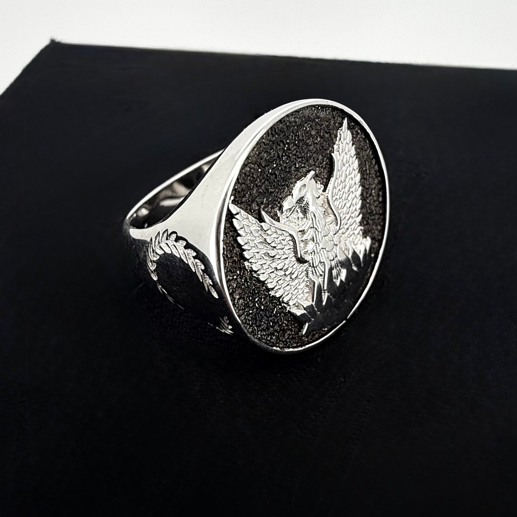 A close up shot of a falcon crest signet ring in silver on a black and white background