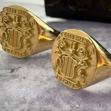 close up photo of 2 yellow gold family crest signet rings on a grey textured background