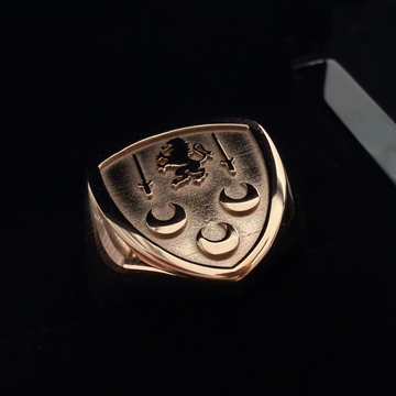 This is a close up top angle shot of a rose gold custom family crest ring , placed inside a black ring box