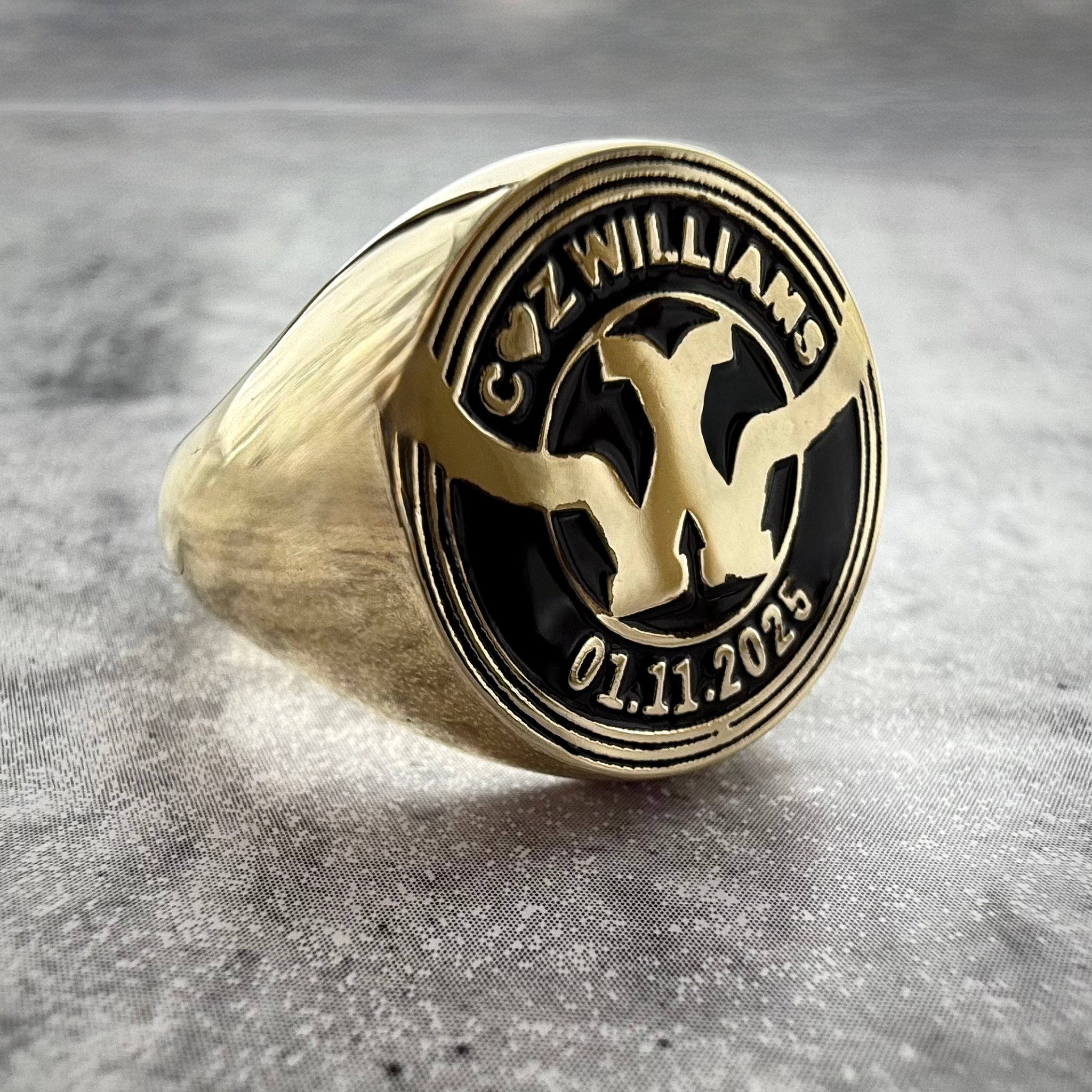 a close up photo of a Custom Gold signet ring with engraved design on a gray textured background