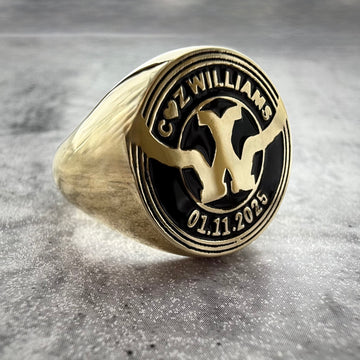 a close up photo of a Custom Gold signet ring with engraved design on a gray textured background