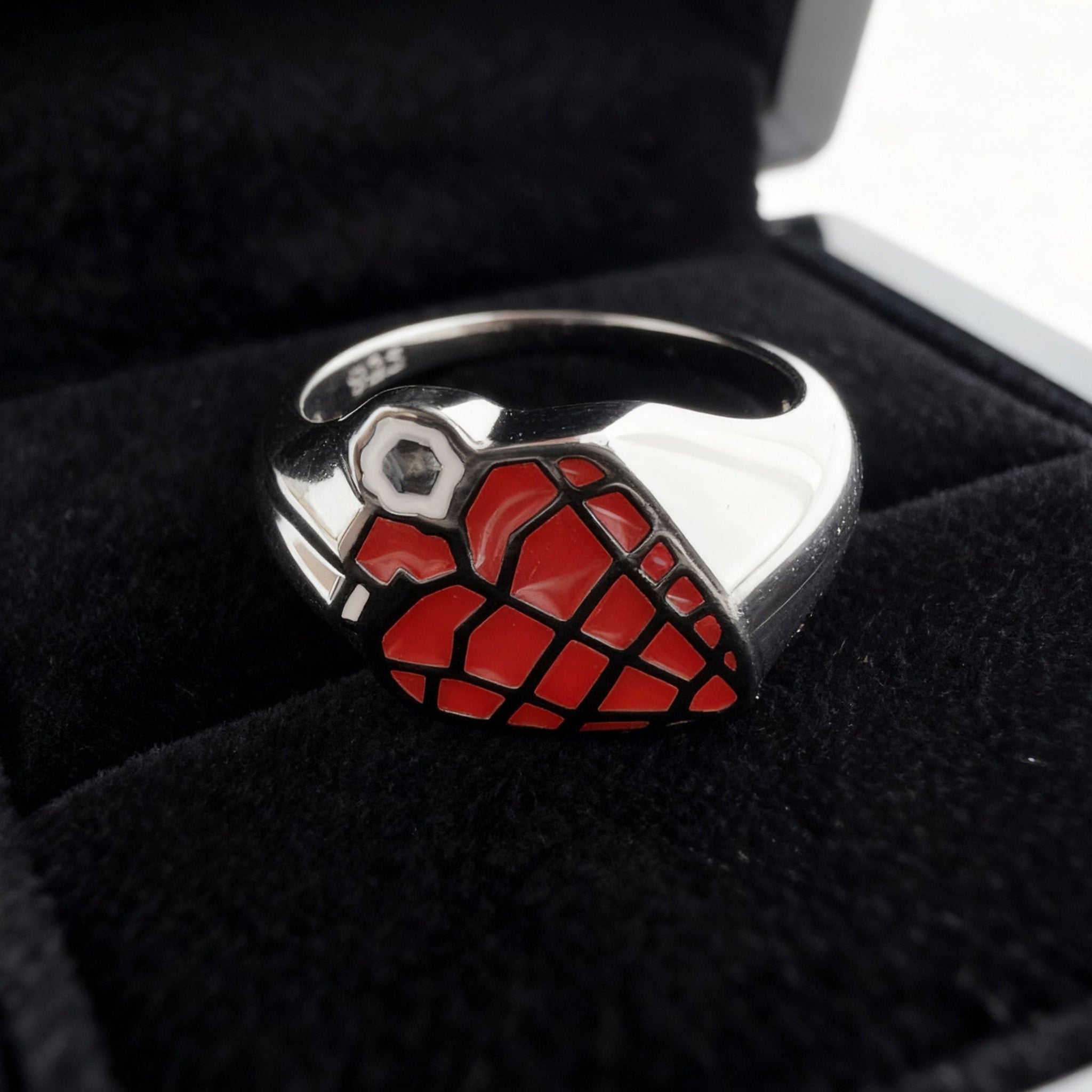 Close up eye-level shot of a custom red and black enamel grenade shape signet ring please on the inside of a black velvet ring box pad
