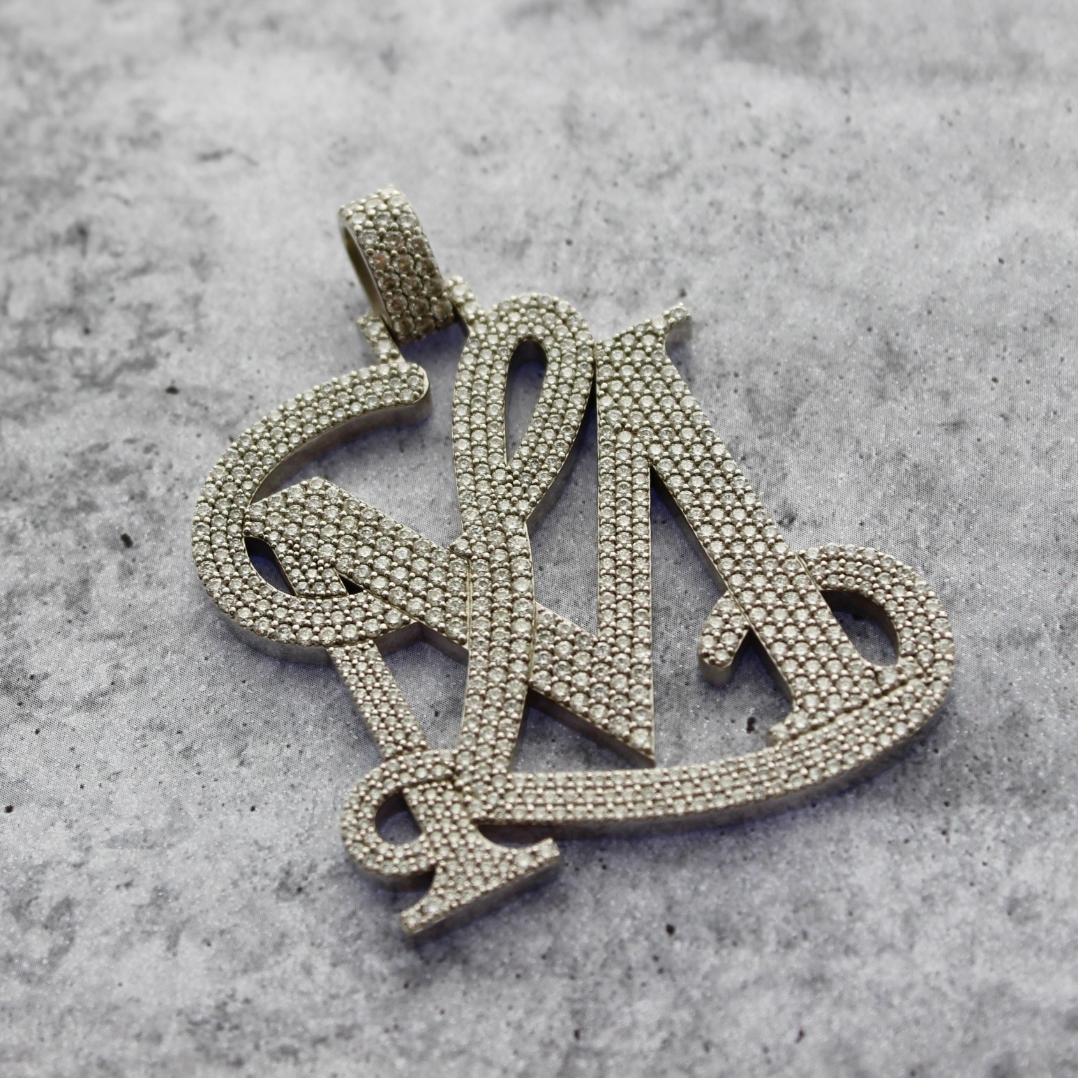 A close up top angle picture of a custom diamond logo pendant. on a grey textured background.