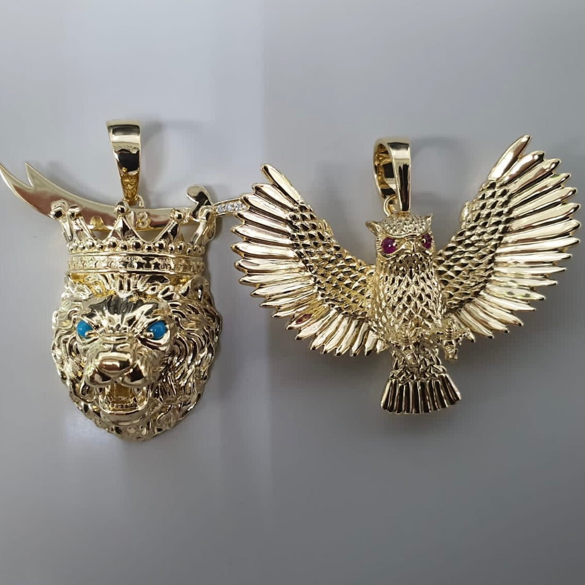 Close up top angle shot of a custom yellow gold lion and next to a custom owl pendant, on a cream background.