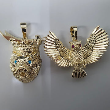 Close up top angle shot of a custom yellow gold lion and next to a custom owl pendant, on a cream background.