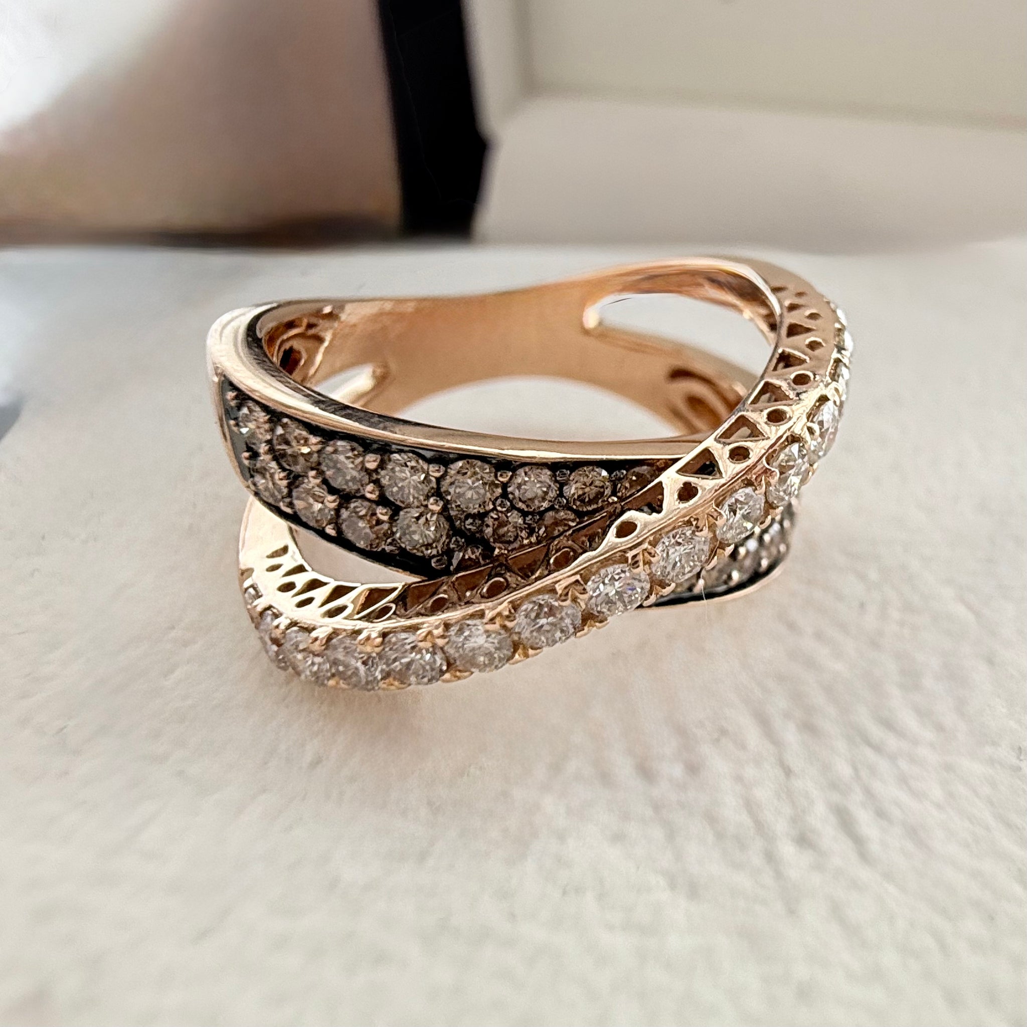 Close up shot of a custom champagne diamond cross over fancy ring in 18k rose gold laid on a cream textured background