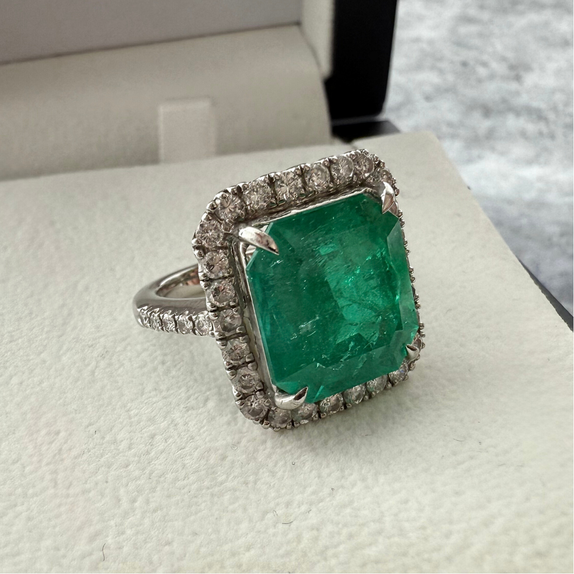 front angle shot of a custom emerald gemstone ring in 18k white gold, with the background being cream colour with texture