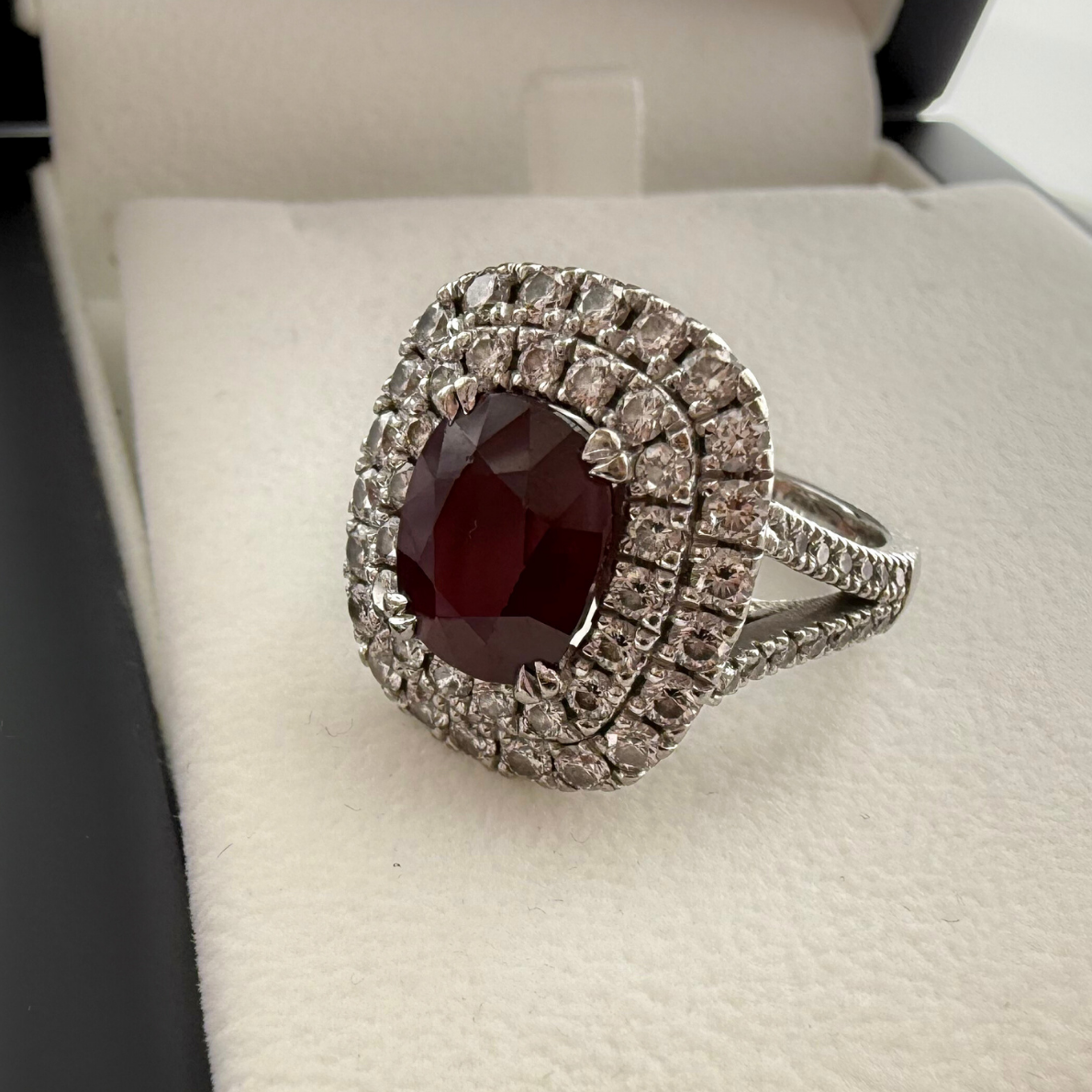 Close up side shot of a custom fancy ruby and white diamond cluster ring laid on a cream textured background