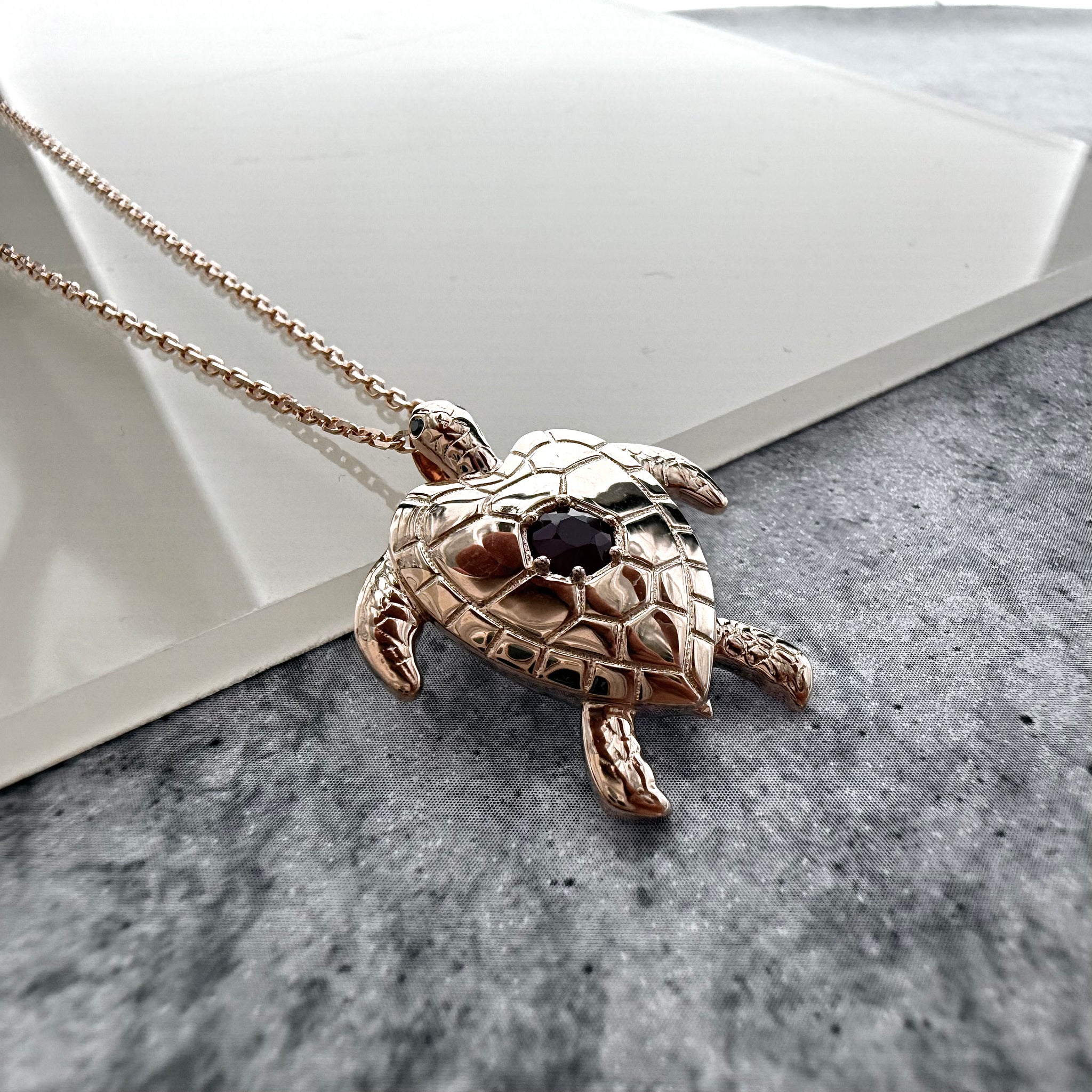 top view close up shot of a custom turtle pendant in rose gold with a deep red ruby on the back of the turtle.