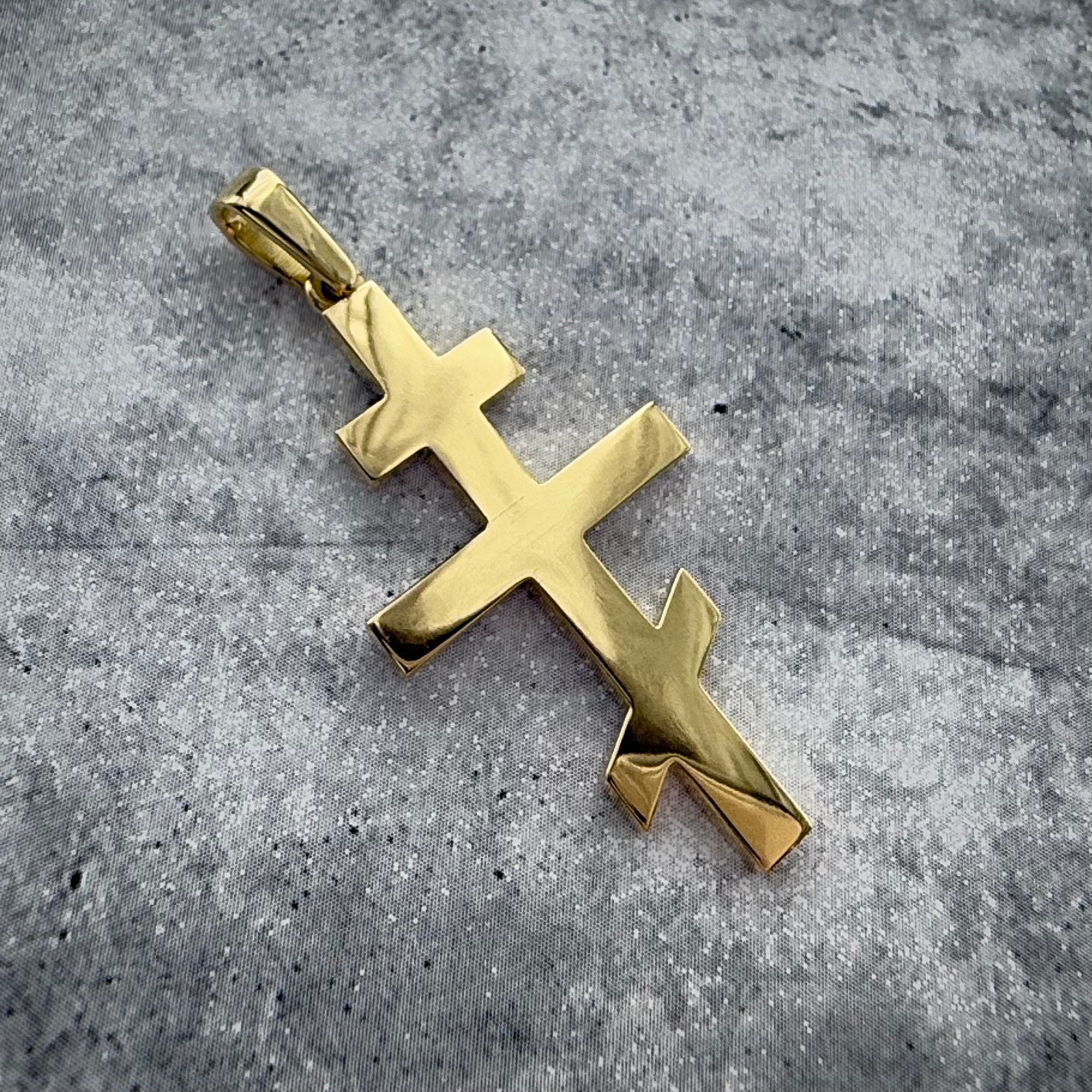 a top angle shot of a custom yellow gold russian orthodox cross pendant, on a grey textured backround.