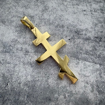 a top angle shot of a custom yellow gold russian orthodox cross pendant, on a grey textured backround.