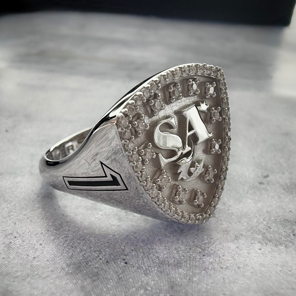 A Close up shot of a Initial signet ring in white gold on a grey textured background