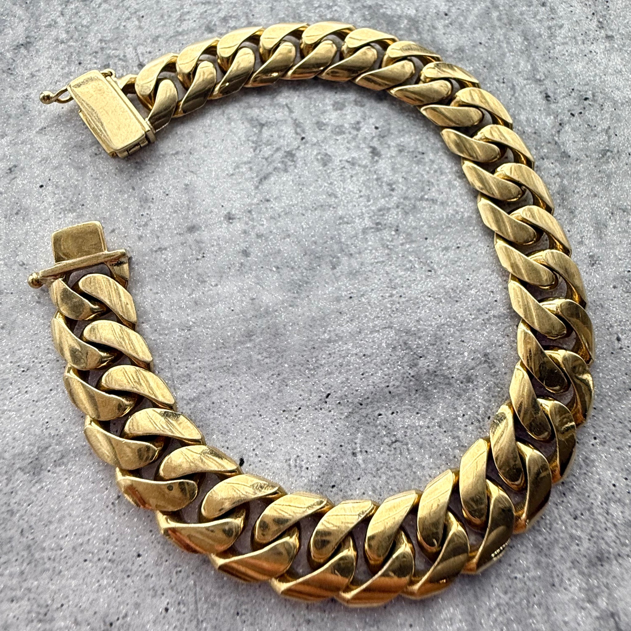Top angle shot of a custom solid 9k yellow gold cuban bracelet on a grey textured background