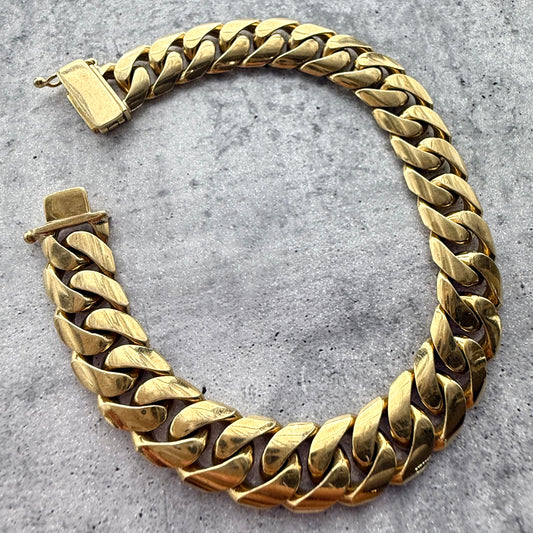 Top angle shot of a custom solid 9k yellow gold cuban bracelet on a grey textured background