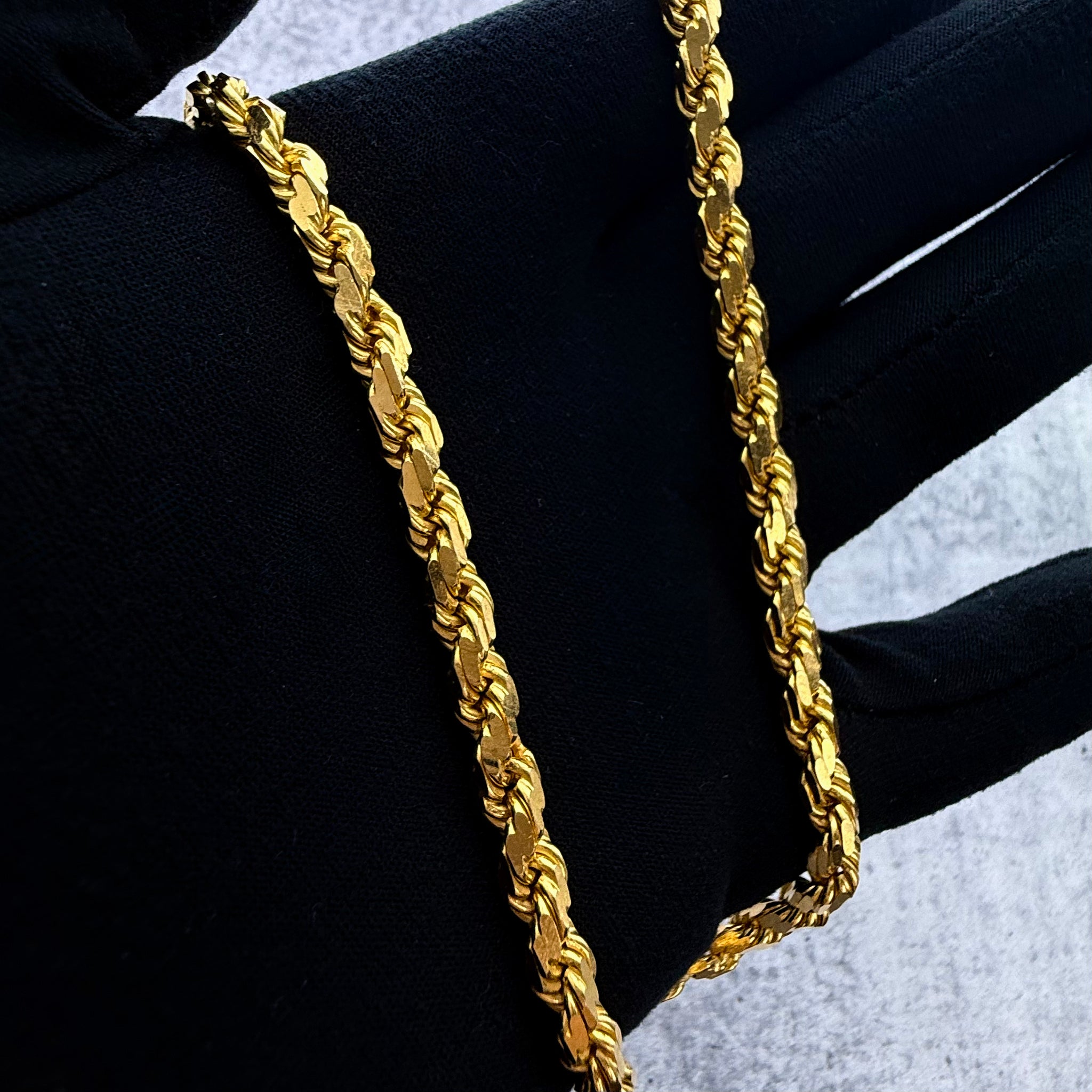a close up front shot of a custom made 22ct rope chain being held in a hand wearing a black glove.