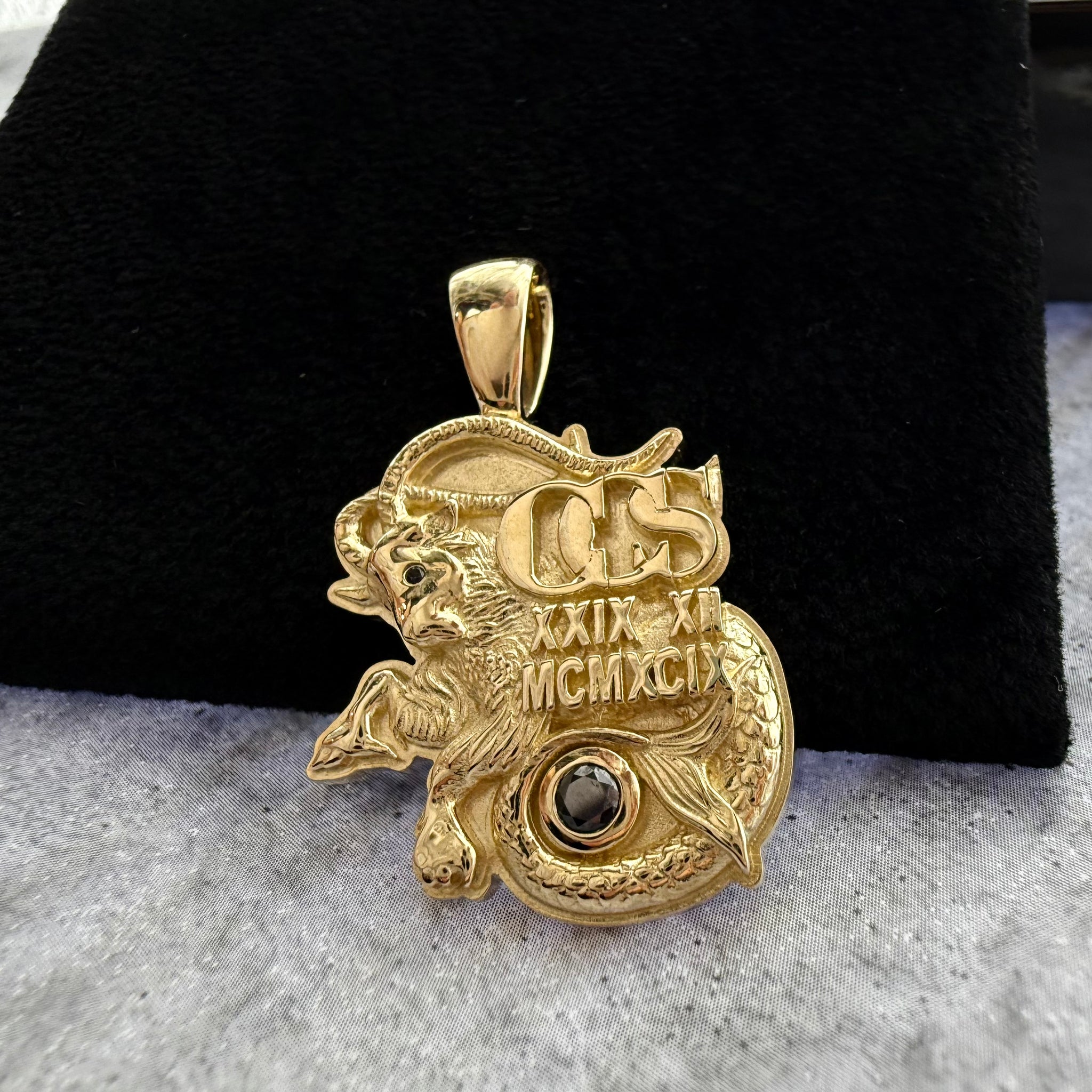 front angle photo of a custom capricorn pendant in yellow gold, with a black and textured grey background
