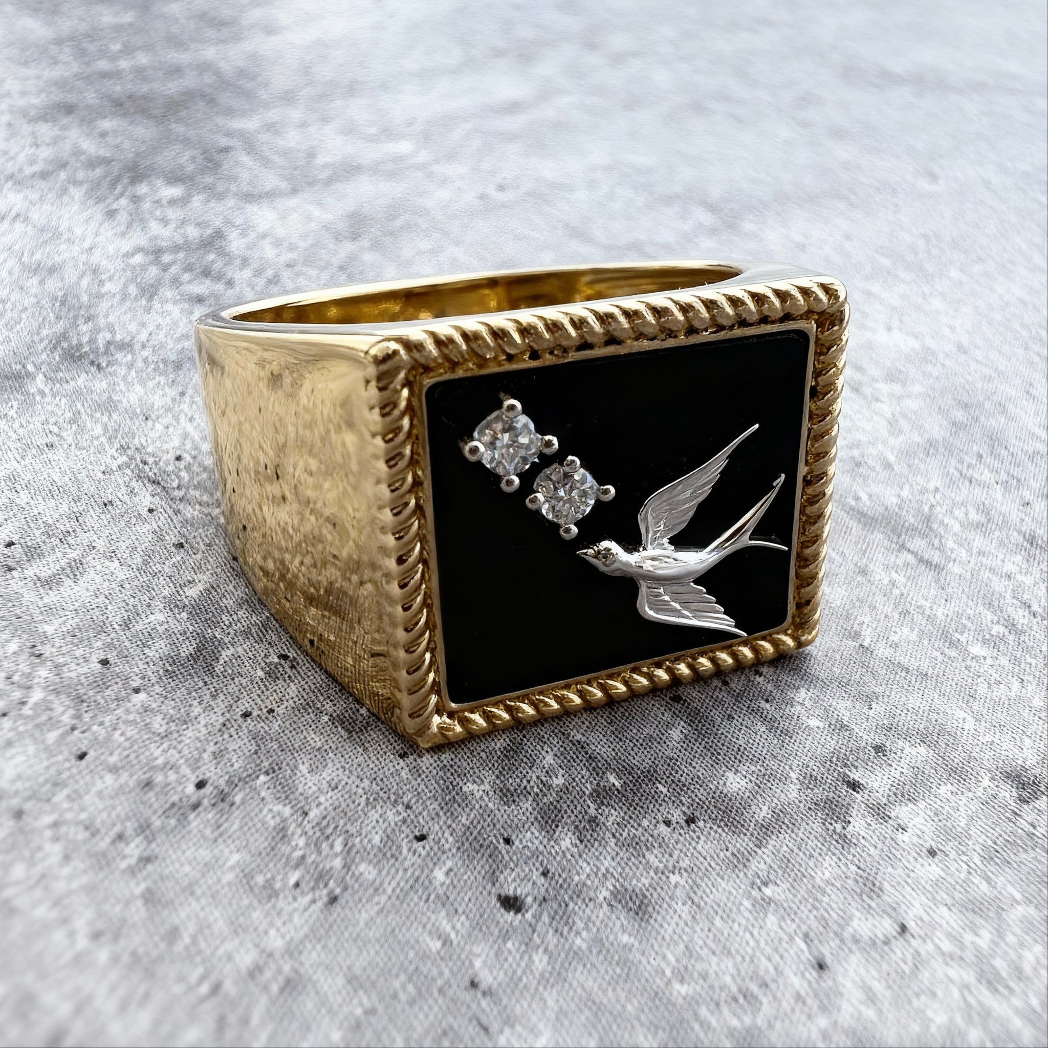 Custom Gold Signet ring ring with black stone featuring a bird and two diamonds on a textured gray surface