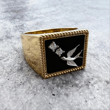Custom Gold Signet ring ring with black stone featuring a bird and two diamonds on a textured gray surface