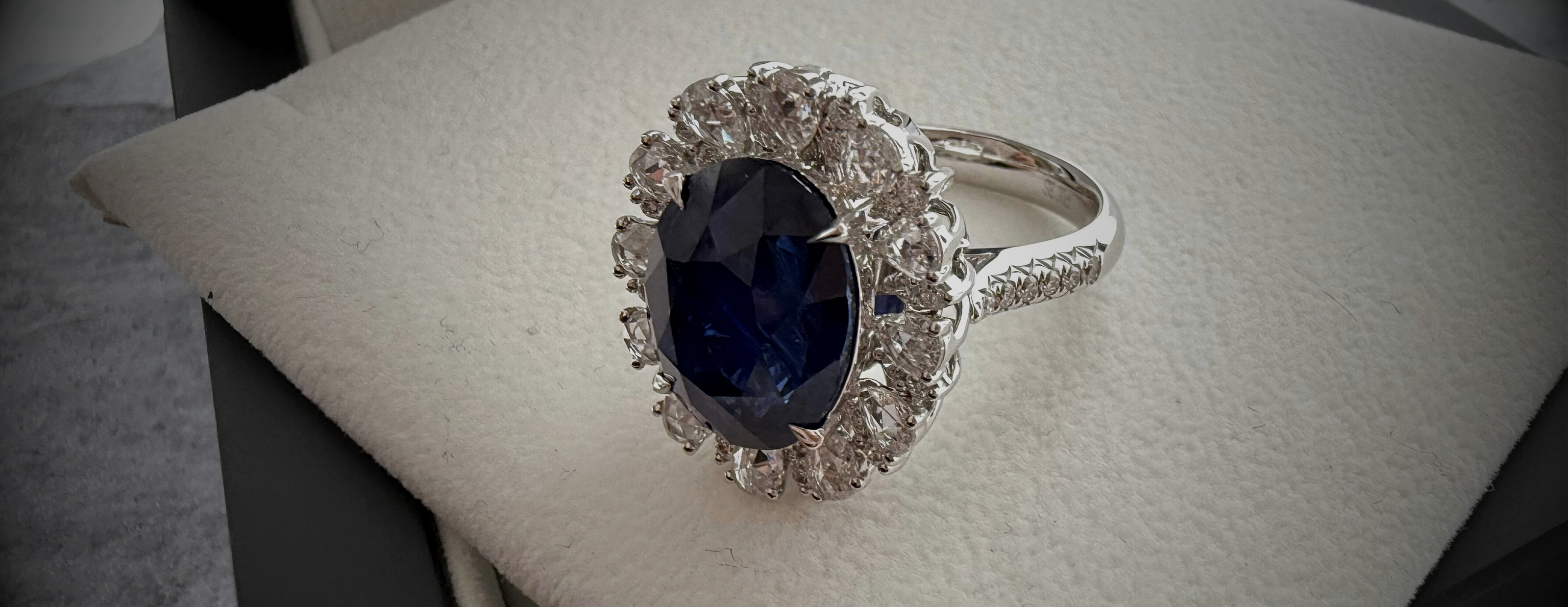 Large banner of a single sapphire and diamond halo ring in 18k white gold laid on a cream textured background