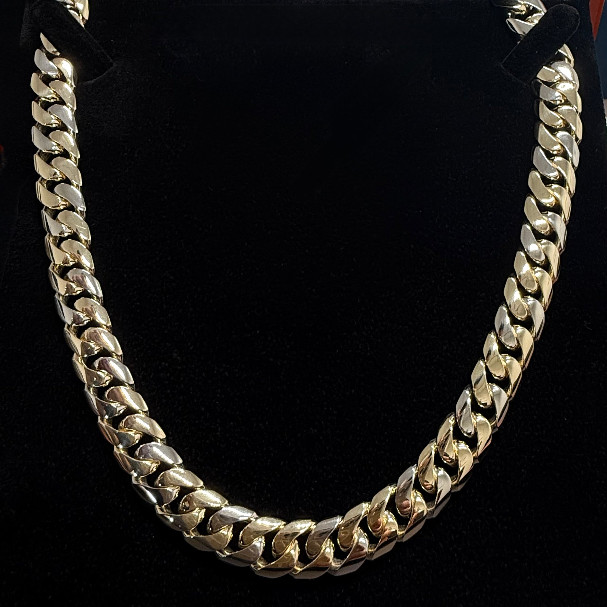 Front on shot of a custom 12mm cuban link chain in solid 9k gold on. a black background
