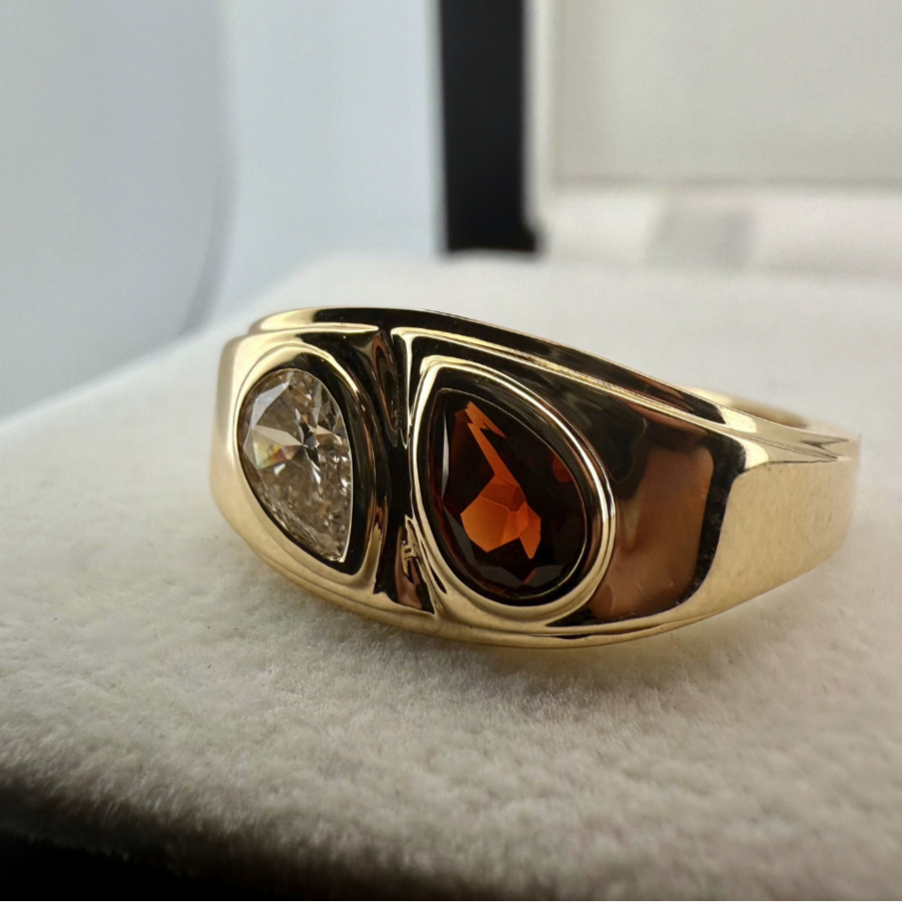 A close up shot of a custom gemstone ring in 18k yellow gold laid on a cream textured background